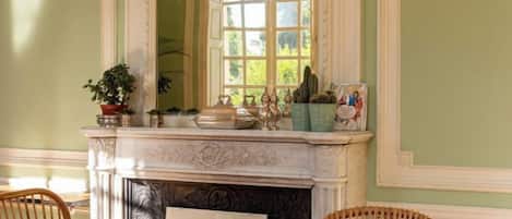 A dining area with a fireplace, a table, chairs, and a window with a view of greenery.