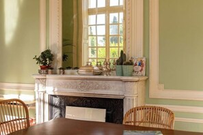 A dining area with a fireplace, a table, chairs, and a window with a view of greenery.