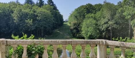A stone balustrade overlooking a pathway through a lush green park.