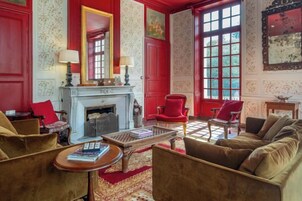 Una habitación con chimenea, sillones rojos, un sofá y una mesa con libros.