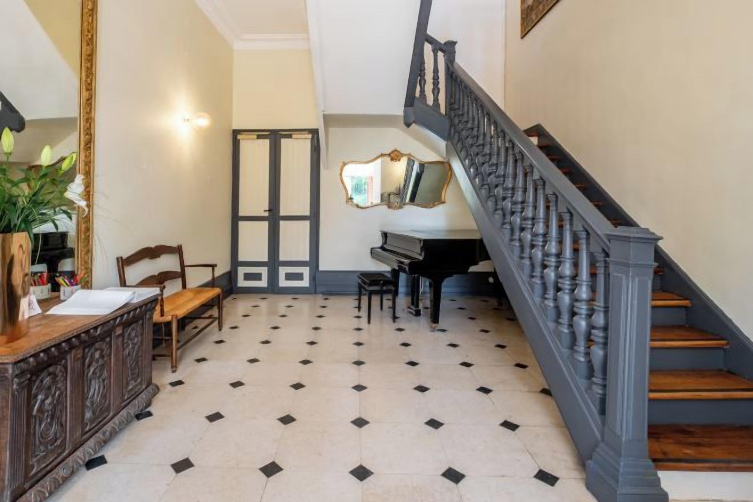 Uma imponente escadaria com guarda-corpo escuro que leva a um piano e um espelho na parede.