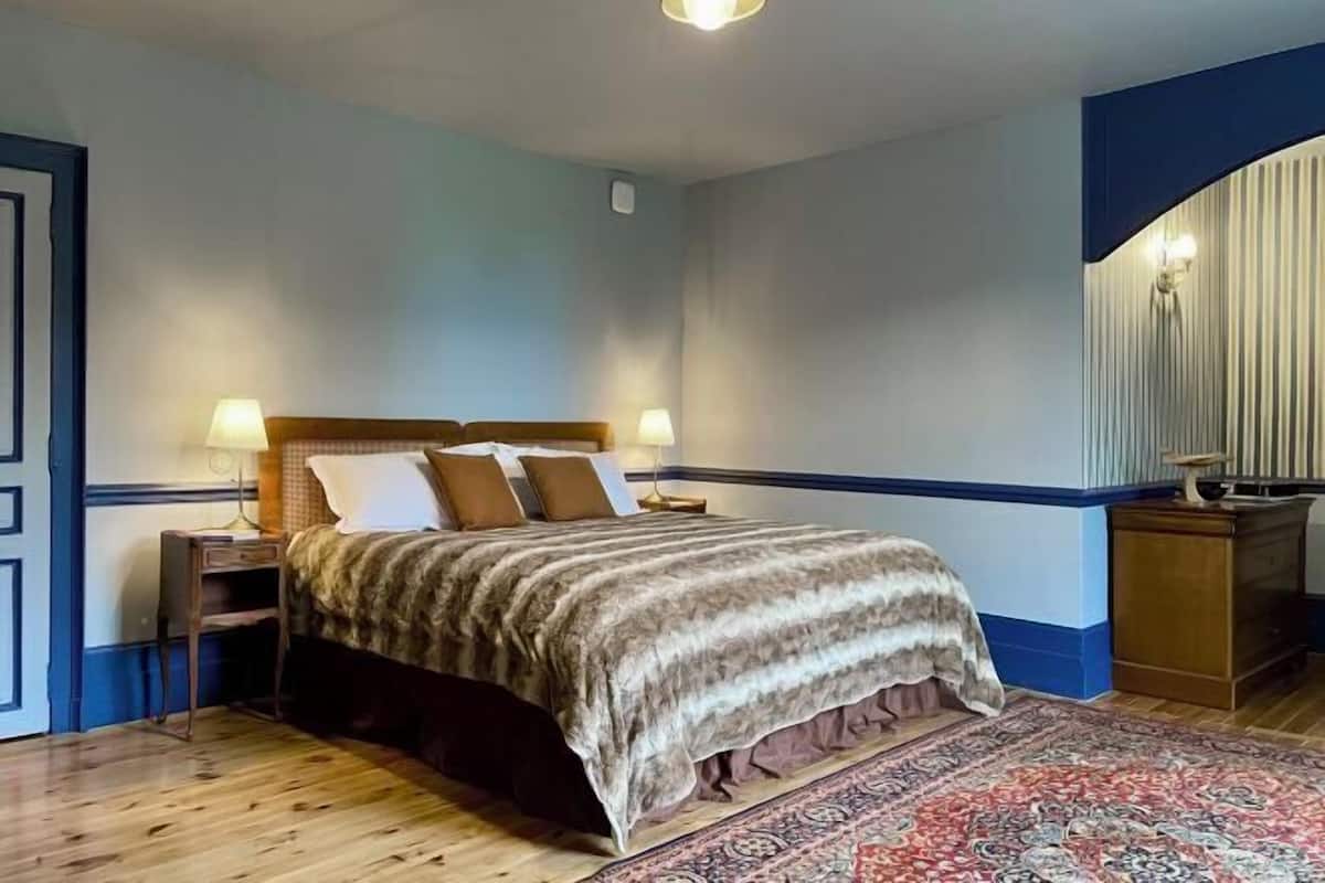 A bedroom with a bed, nightstands, a rug, and a wall-mounted light fixture.