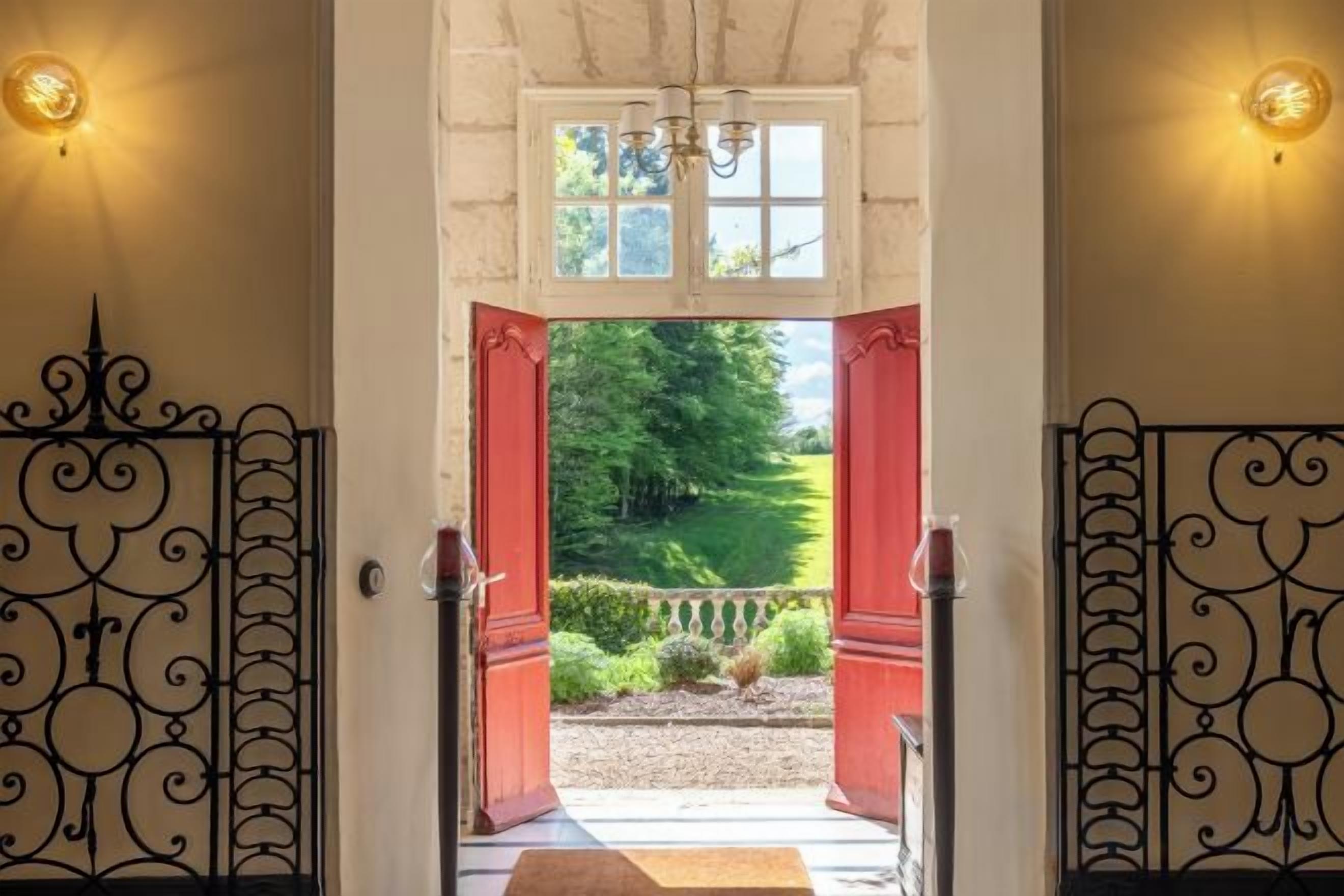 Uma porta com portão de ferro forjado, um pequeno degrau que dá para um jardim, e uma janela sobre a porta.