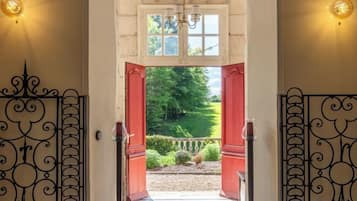 Une porte surmontée d’un portail en fer forgé, une petite marche menant à un jardin, et une fenêtre au-dessus de la porte.