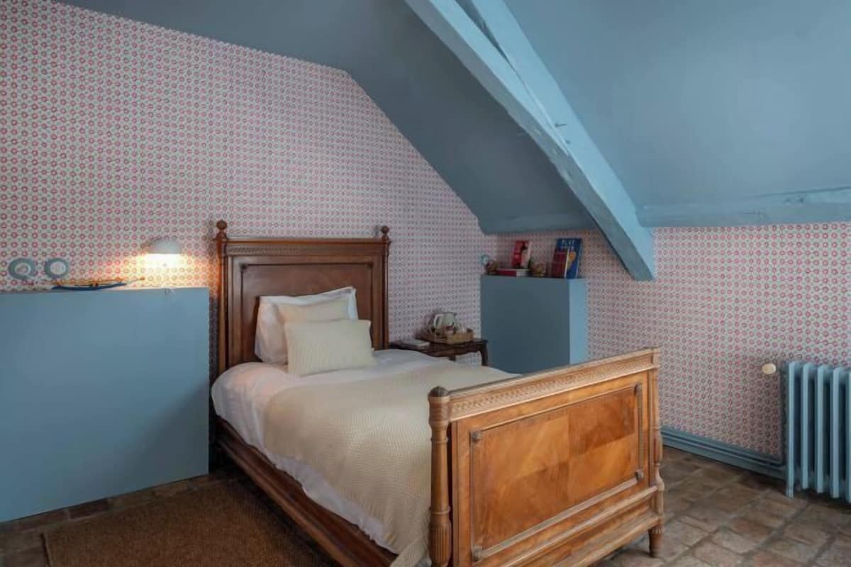 A bedroom with a wooden bed, a nightstand, a radiator, and patterned wallpaper.