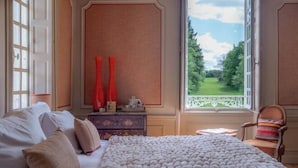 A bedroom with a large bed, a dresser, a chair, and a view of a green landscape through a window. - Huberdière Castle (Nazelles-Negron)