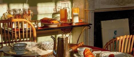 A breakfast table with various breakfast items, a kettle, and a fireplace in the background.