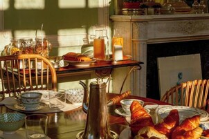Una mesa de desayuno con diversos alimentos, una tetera y una chimenea al fondo.