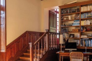 Een trap met houten spijlen, een boekenplank vol boeken en een bureau met een computer.