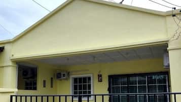A yellow building with a covered entrance, a black metal gate, and air conditioning units.