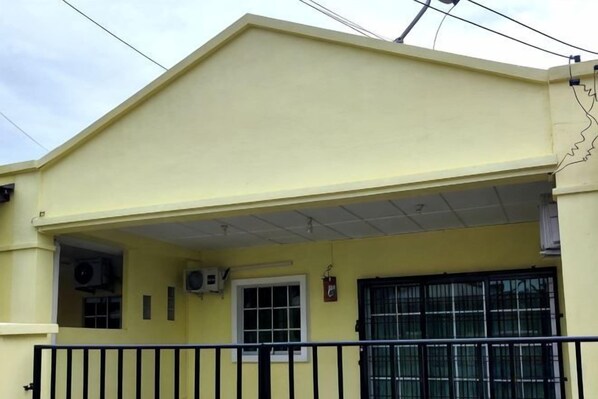 Un bâtiment jaune avec une entrée couverte, un portail en métal noir et des unités de climatisation.