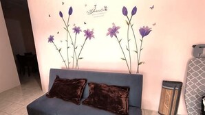 A blue sofa with two dark cushions, a wall with purple flowers, and a trash can.