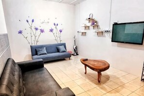 A living room with a sofa, a coffee table, a TV, and a decorative wall.