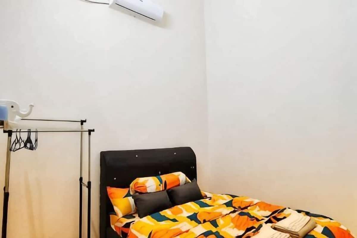 Ein Einzelbett mit gemustertem Bettbezug, ein Nachttisch und eine Wand-Klimaanlage.