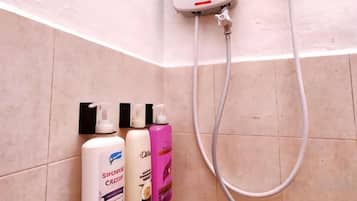 A bathroom with a shower head, a towel rack, and two bottles of shampoo.