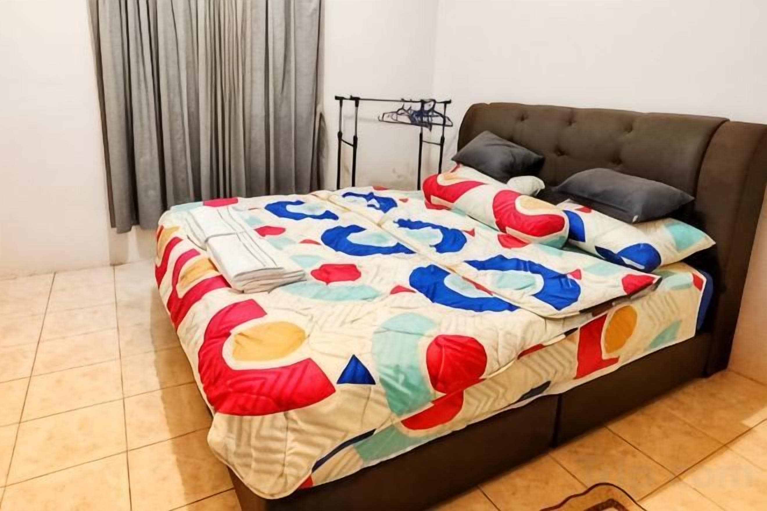 A bed with a colorful quilt, a dark sofa, and a small table with a lamp.