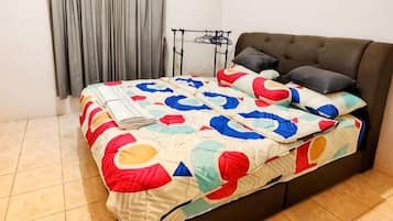 A bed with a colorful quilt, a dark sofa, and a small table with a lamp.