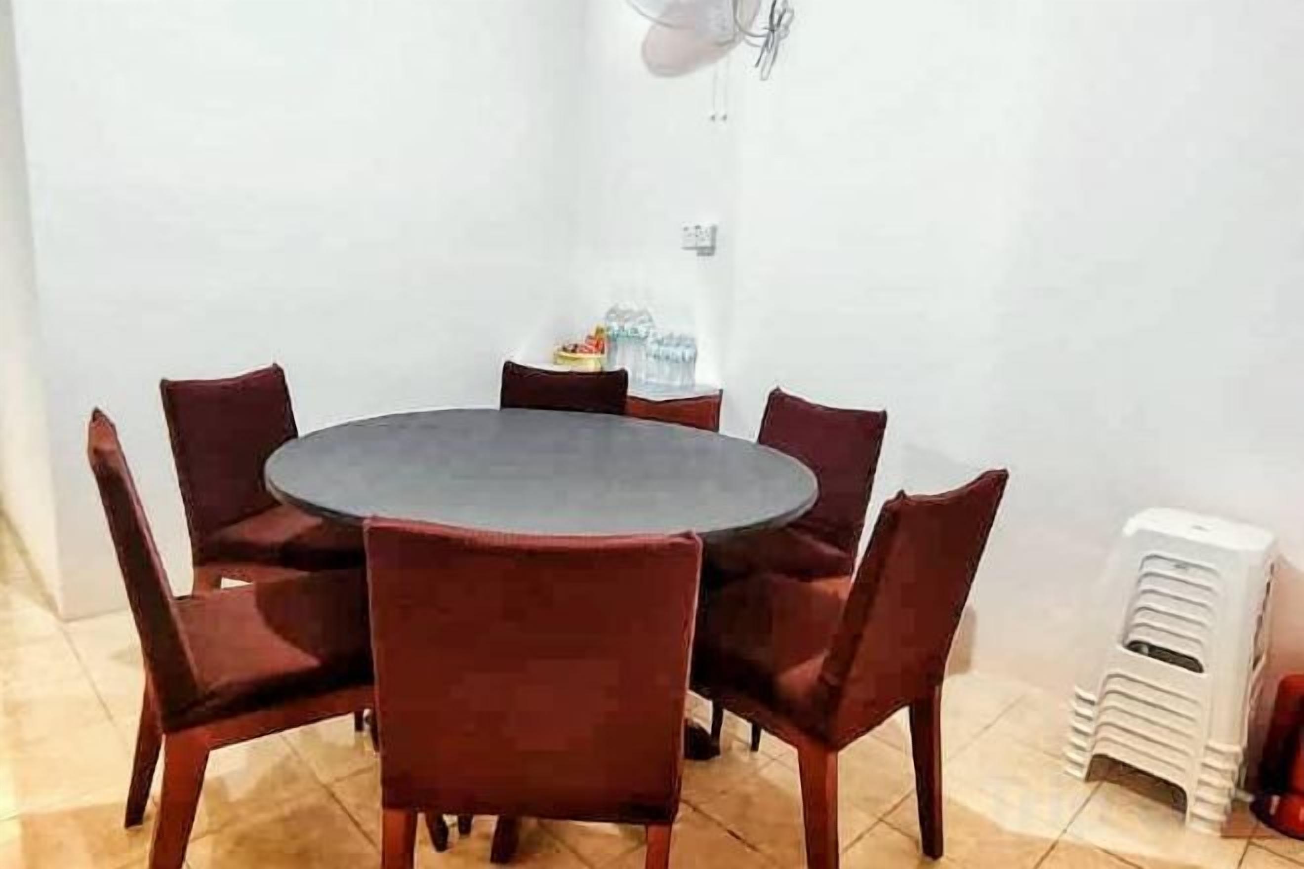 A round table with six chairs, a small table with a lamp, and a white wall.