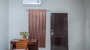 A room with a wooden table, a chair, a small potted plant, a dark door, and a light-colored wall. - Amor Homestay near Eltari International Airport Mitra RedDoorz (Liliba)