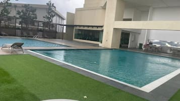 A swimming pool with a grassy area and lounge chairs, surrounded by a building with large windows and a balcony.
