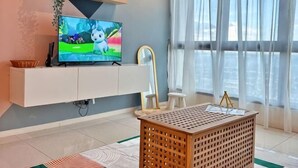 En moderne stue med et fladskærms-tv, et hvidt tv-møbel og et stort vindue med let gardin.