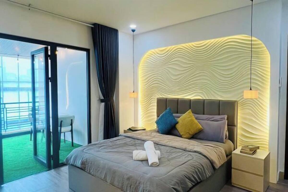 A modern hotel room with a large bed, a nightstand, a lamp, and a view of a balcony.