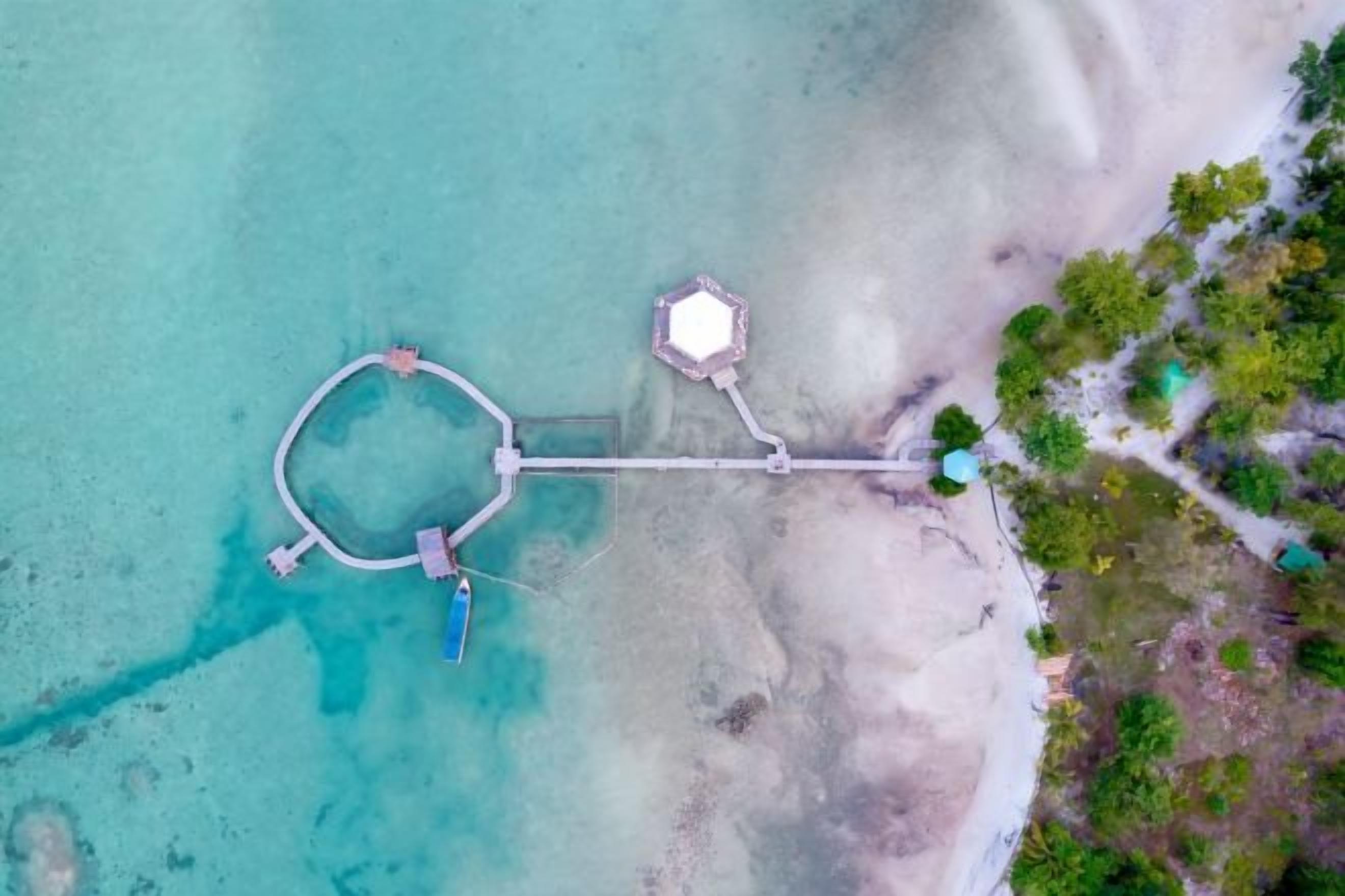 An aerial view of a coastal area with a circular water body, a pier, and a small building.