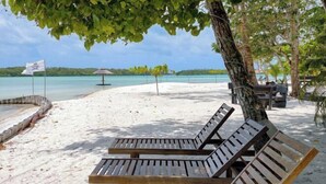 A beach with wooden lounge chairs, a flag, and a clear view of the ocean.