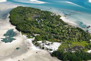 An aerial view of a coastal area with a beach, dense forest, and a small settlement with visible buildings and boats. - Leebong Island (Pegantungan)