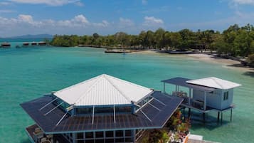 A resort with overwater bungalows, clear turquoise water, and a forested island in the background.