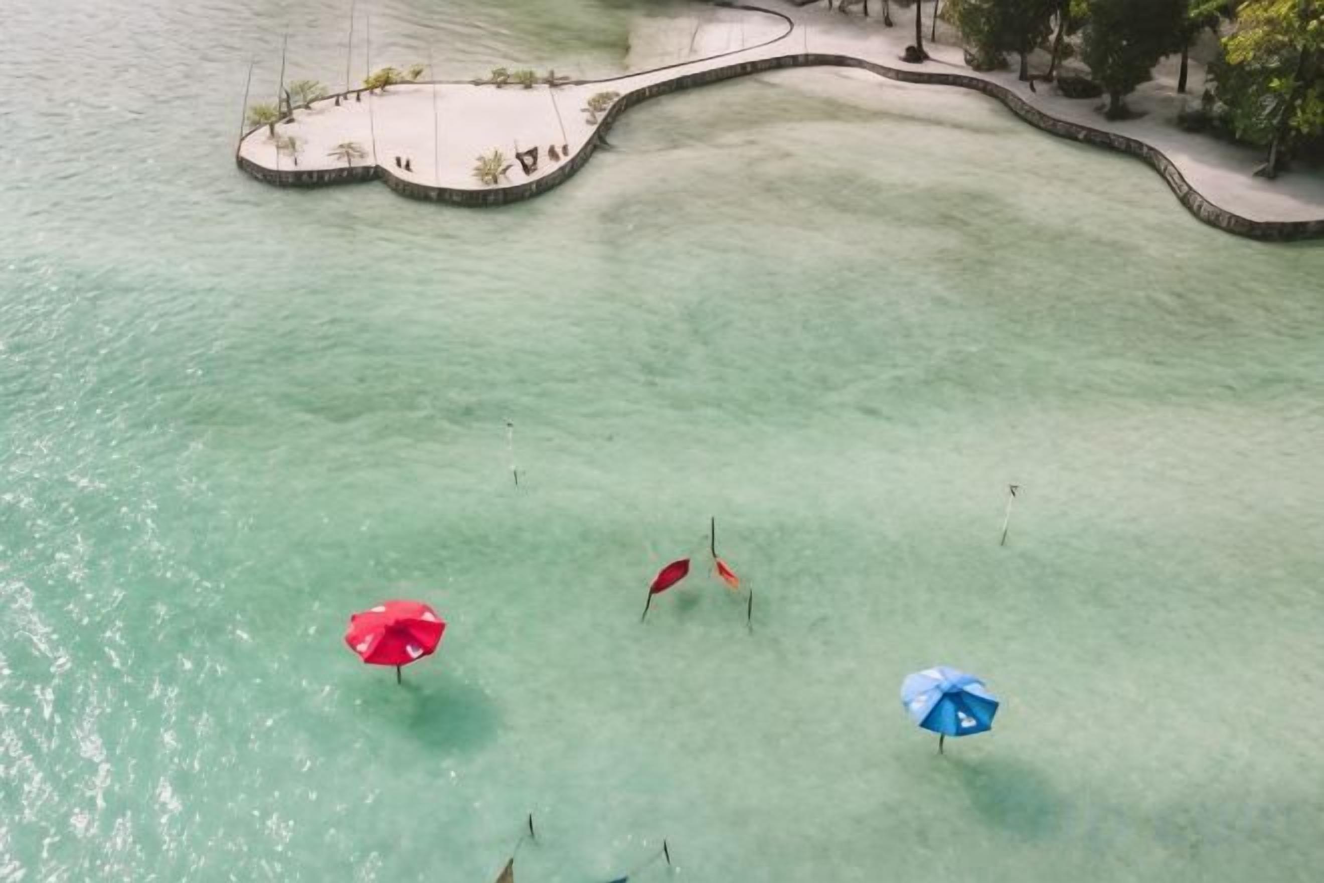 A clear view of a beach with three umbrellas, a pathway, and a small island with a dock.