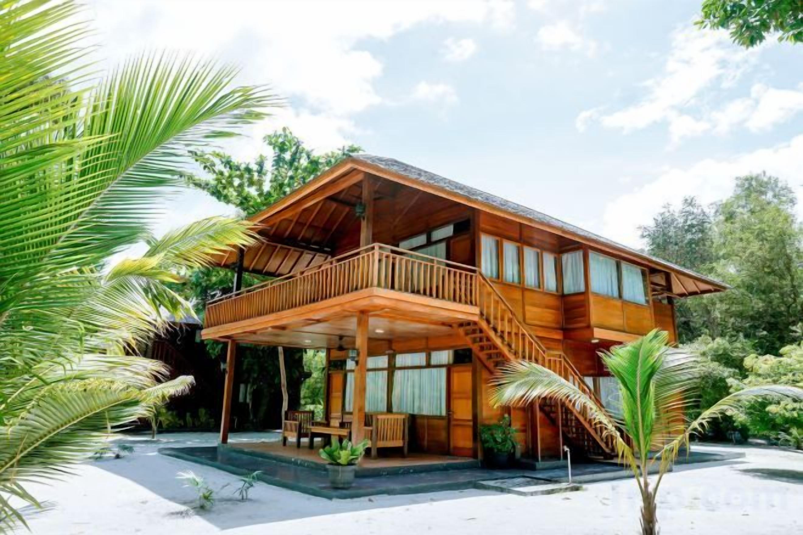 A wooden house with a balcony, surrounded by palm trees and greenery.