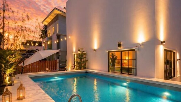 A modern pool area with a clear pool, a white building with exterior lighting, and a wooden deck. - Luxury Private Pool Villa "Psalms 23 Residence @Huaikwang" (Bangkok)