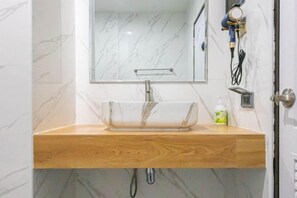 A bathroom with a marble wall, a wooden vanity, a glass sink, a handheld hair dryer, and a bottle of shampoo. - Luxury Private Pool Villa "Psalms 23 Residence @Huaikwang" (Bangkok)