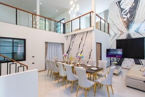 A spacious living area with a high ceiling, a dining table set for six, and a flat-screen TV mounted on the wall. - Luxury Private Pool Villa "Psalms 23 Residence @Huaikwang" (Bangkok)