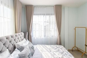 A bedroom with a tufted headboard, a bed with patterned bedding, and a window with sheer curtains. - Luxury Private Pool Villa "Psalms 23 Residence @Huaikwang" (Bangkok)