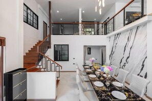 A spacious dining area with a long table set for multiple people, a staircase leading to an upper level, and a modern interior design. - Luxury Private Pool Villa "Psalms 23 Residence @Huaikwang" (Bangkok)