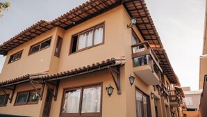 A multi-story building with a tiled roof, multiple windows, and balconies. - Apartamento Novo ao lado da Rua Mucugê (Porto Seguro)