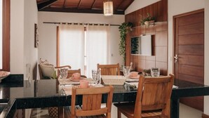A dining area with a black marble table, wooden chairs, and a hanging light fixture. - Apartamento Novo ao lado da Rua Mucugê (Porto Seguro)