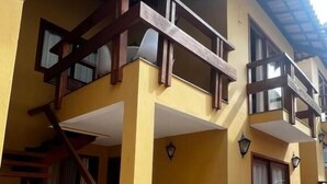A two-story building with a wooden staircase leading to a balcony. - Apartamento Novo ao lado da Rua Mucugê (Porto Seguro)
