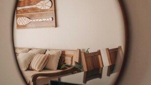 A round mirror reflecting a cozy living room with a sofa, cushions, and a wooden wall art piece. - Apartamento Novo ao lado da Rua Mucugê (Porto Seguro)