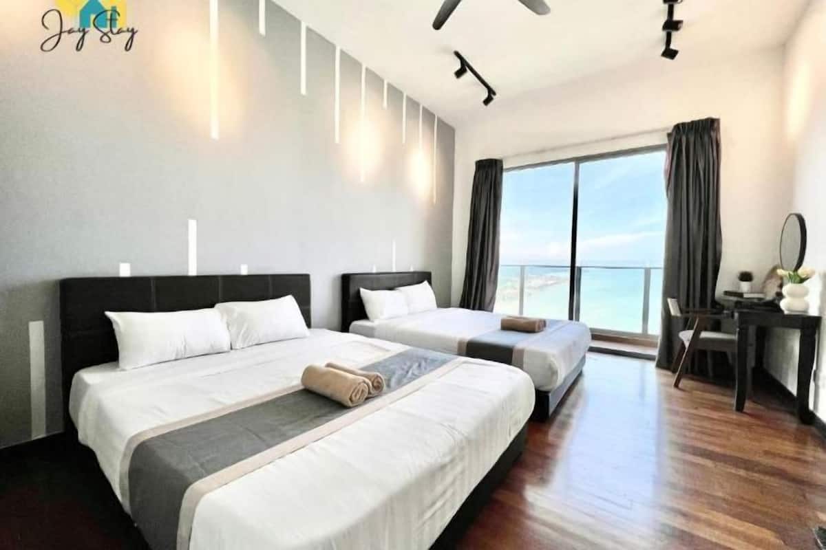 Een hotelkamer met twee bedden, een bureau, een stoel en een groot raam met uitzicht op zee.