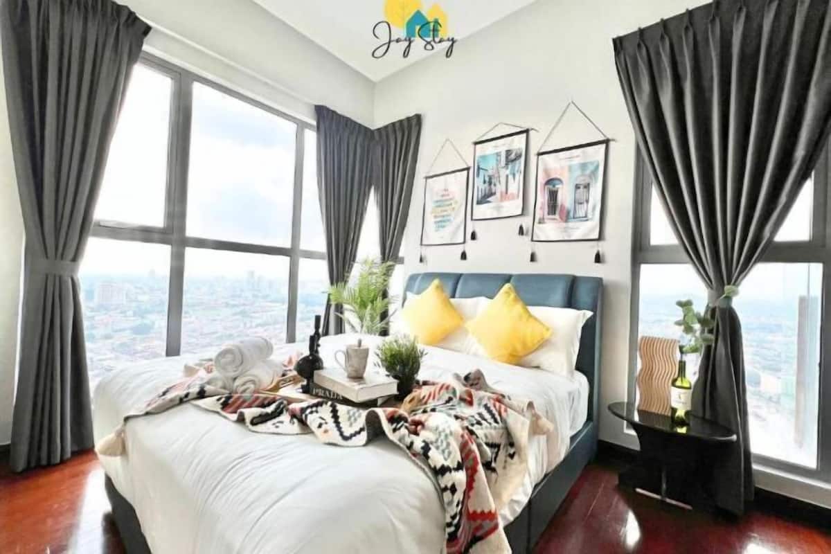 Hotelkamer met een groot bed, uitzicht op de stad, ingelijste foto’s aan de muur en een klein bijzettafeltje met een plant.