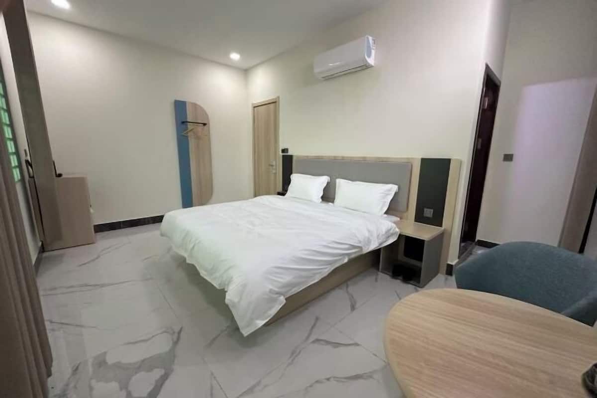 A hotel room with a bed, bedside table, chair, and an air conditioning unit.
