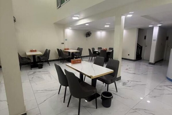 A hotel dining area with tables and chairs, a trash bin, and a ceiling fan. - zhuo' bo hotel (Ta Khmau)