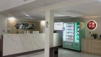 Un espace d’accueil avec un comptoir en marbre, un distributeur automatique vert et un panneau fixé au mur.