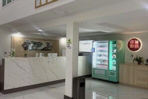 Un espace d’accueil avec un comptoir en marbre, un distributeur automatique vert et un panneau fixé au mur.