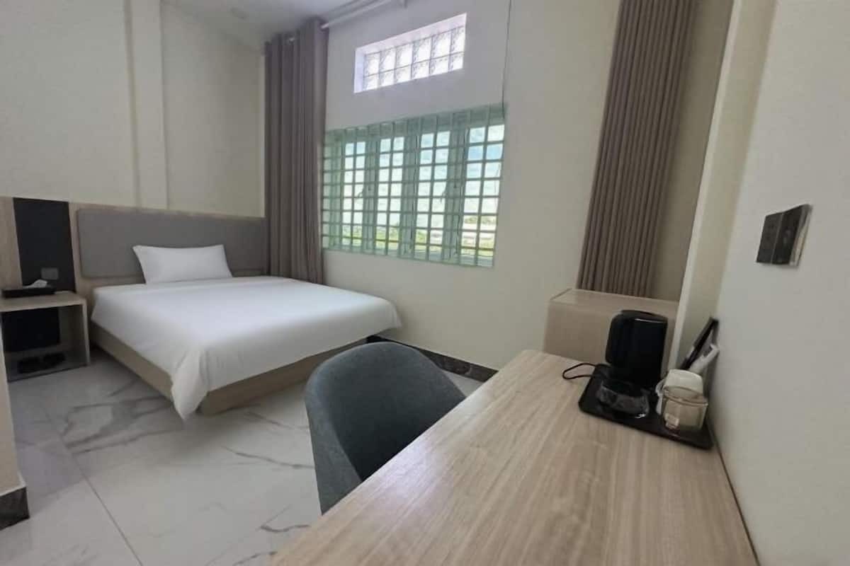 A hotel room with a bed, a desk, a chair, a coffee maker, and a window with curtains.