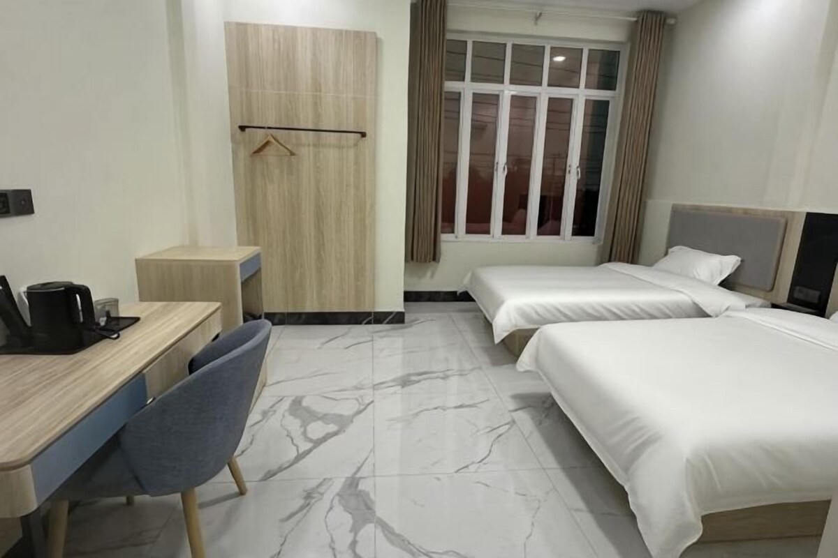 A hotel room with a desk, two beds, a wardrobe, and a window with curtains.