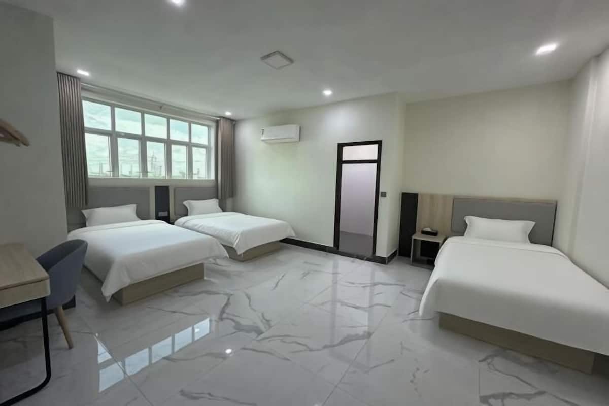 A hotel room with two beds, a desk, a chair, a window, and a door.